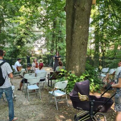 Letnie czytanie w Lubniewicach. Publiczność siedząca i stojaca w cieniu parkowych drzew. Kliknięcie powoduje powiększenie zdjęcia