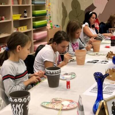 Dziewczynki w skupieniu malują wazy. Widać na zdjęciu różne postępy pracy. Kliknięcie powoduje powiększenie zdjęcia
