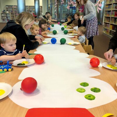 Dzieci siedzą przy stole i za pomocą drewnianych patyczków mieszają farby na talerzykach. Kolejnym etapem ich pracy plastycznej będzie malowanie balonem po kartce wyciętej w kształt gąsienicy.