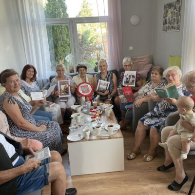 Grupa uczestników trzymających książki „Nad Niemnem" siedząca przy stoliku z poczęstunkiem. Kliknięcie powoduje powiększenie zdjęcia.