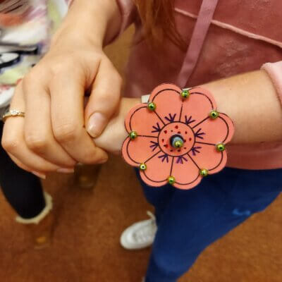 Nadgarstek dziewczyny z wykonaną papierową bransoletką w formie kwiatka z przyklejonymi koralikami. Kliknięcie powoduje powiększenie zdjęcia.