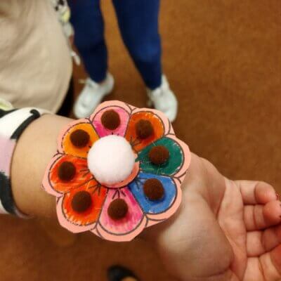 Nadgarstek dziewczyny z wykonaną papierową bransoletką w formie kwiatka z przyklejonymi kreatywnymi pomponami. Kliknięcie powoduje powiększenie zdjęcia.