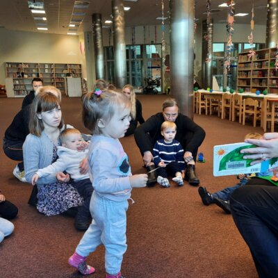 Pani Bibliotekarka czyta dzieciom książeczkę o zielonej bardzo głodnej gąsienicy.