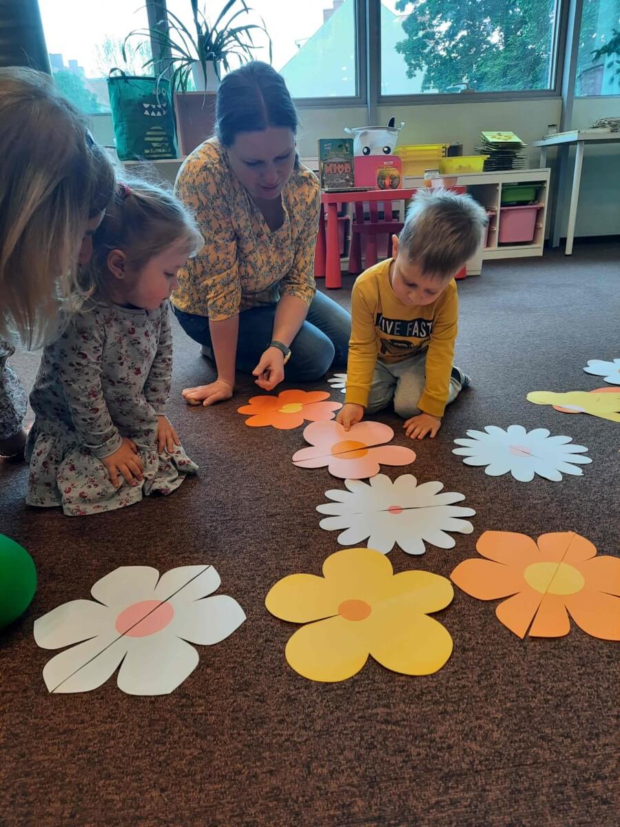 Dzieci przy pomocy opiekunów łączą w pary pocięte kwiatki.