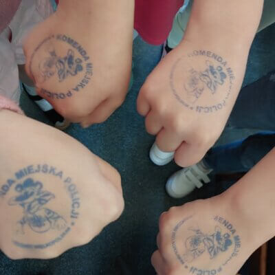 Cztery zaciśnięte dłonie dzieci, na których są pieczątki z nazwą Komenda Miejska Policji.Kliknięcie powoduje powiększenie zdjęcia.