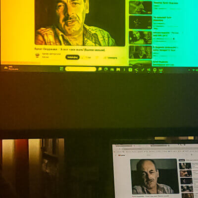 Widoczny rzutnik. Odpalony YouTube. Na ekranie Bułat Okudżawa w koszuli w kratkę. W prawym dolnym rogu widoczny taki sam obraz na ekranie laptopa. Kliknięcie powoduje powiększenie zdjęcia.