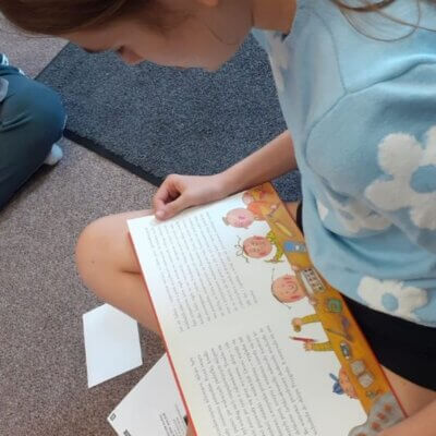 Dziewczynka w niebieskiej bluzce siedzi na dywanie i czyta tekst książki. Kliknięcie powoduje powiększenie zdjęcia.