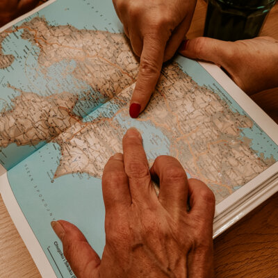 Zbliżenie na książkę. Widoczny fragment mapy Japonii. Palce dłoni dwóch kobiet wskazują niewielką wyspę na środku mapy. Tam mieści się prawdziwe Les Archives du Cœur. Kliknięcie powoduje powiększenie zdjęcia.