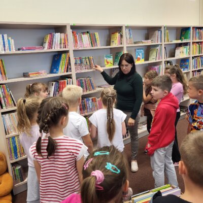 Bibliotekarka wskazuje dzieciom książki do nauki samodzielnego czytania. Kliknięcie powoduje powiększenie zdjęcia.