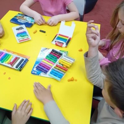 Dzieci siedzą przy żółtym stole. Na stole jest kolorowa plastelina. Kliknięcie w obrazek spowoduje powiększenie.