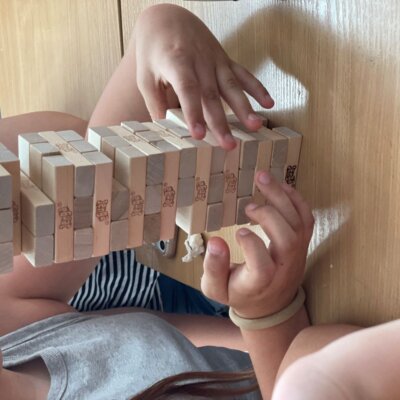 Dziecko przy stole układa klocki w wysoką wieżę - gra Yenga. Kliknięcie powoduje powiększenie zdjęcia.