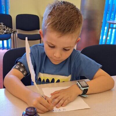 Chłopiec pisze na kartce datę piórem i atramentem. Kliknięcie powoduje powiększenie zdjęcia.