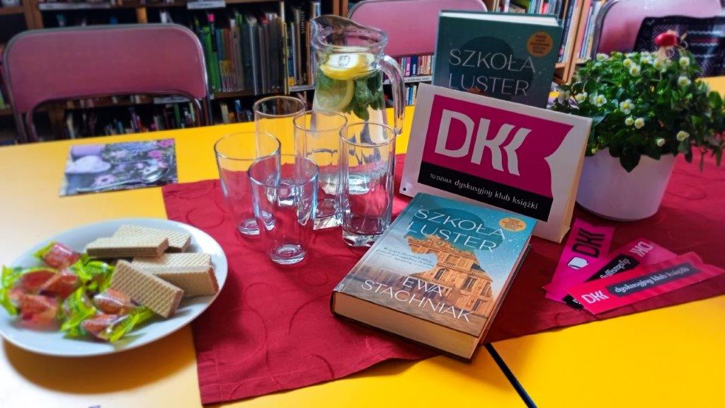 Książki i dzbanek z wodą oraz logo DKK na stole.