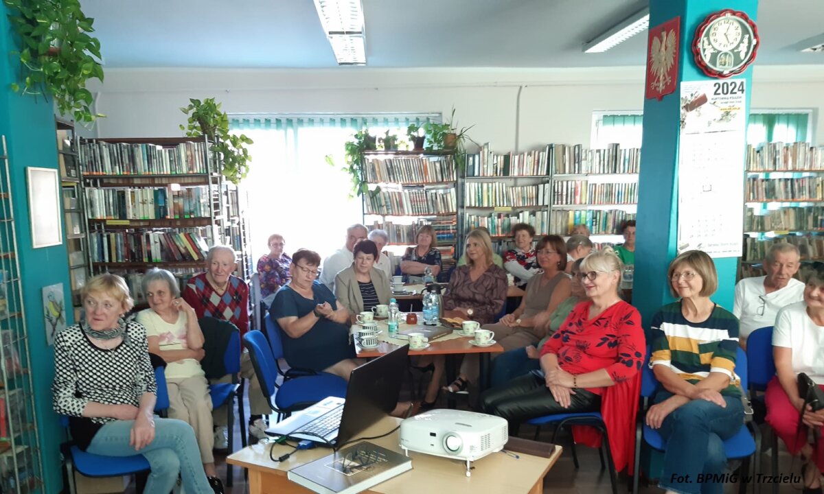 Grupa osób siedzi w pomieszczeniu biblioteki.