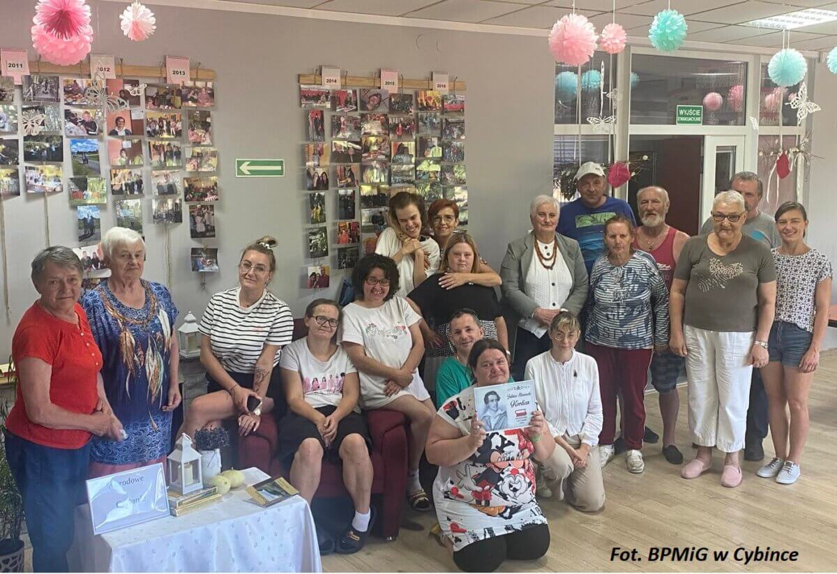 Grupa osób w pomieszczeniu biblioteki prezentująca plakat Narodowego czytania. Kliknięcie powoduje powiększenie zdjęcia.