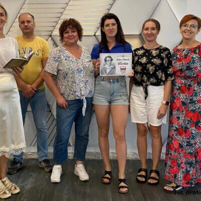 Pięć kobiet i jeden mężczyzna stoją przy ścianie, jedna z kobiet trzyma plakat Narodowego Czytania, druga książkę. Kliknięcie powoduje powiększenie zdjęcia.