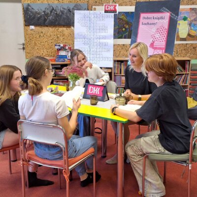 Uczestniczki DKK wraz z bibliotekarką siedzą przy stole, omawiają książkę i śmieją się. Kliknięcie w obrazek spowoduje powiększenie.