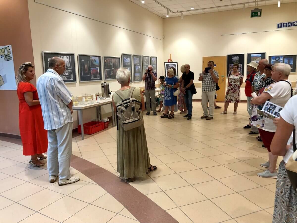 Uczestnicy (mężczyźni i kobiety) podczas otwarcia wystawy w „Galerii Pod Kopułą” na pierwszym piętrze biblioteki. W tle mężczyźni z aparatami fotograficznymi dokumentujący moment otwarcia.