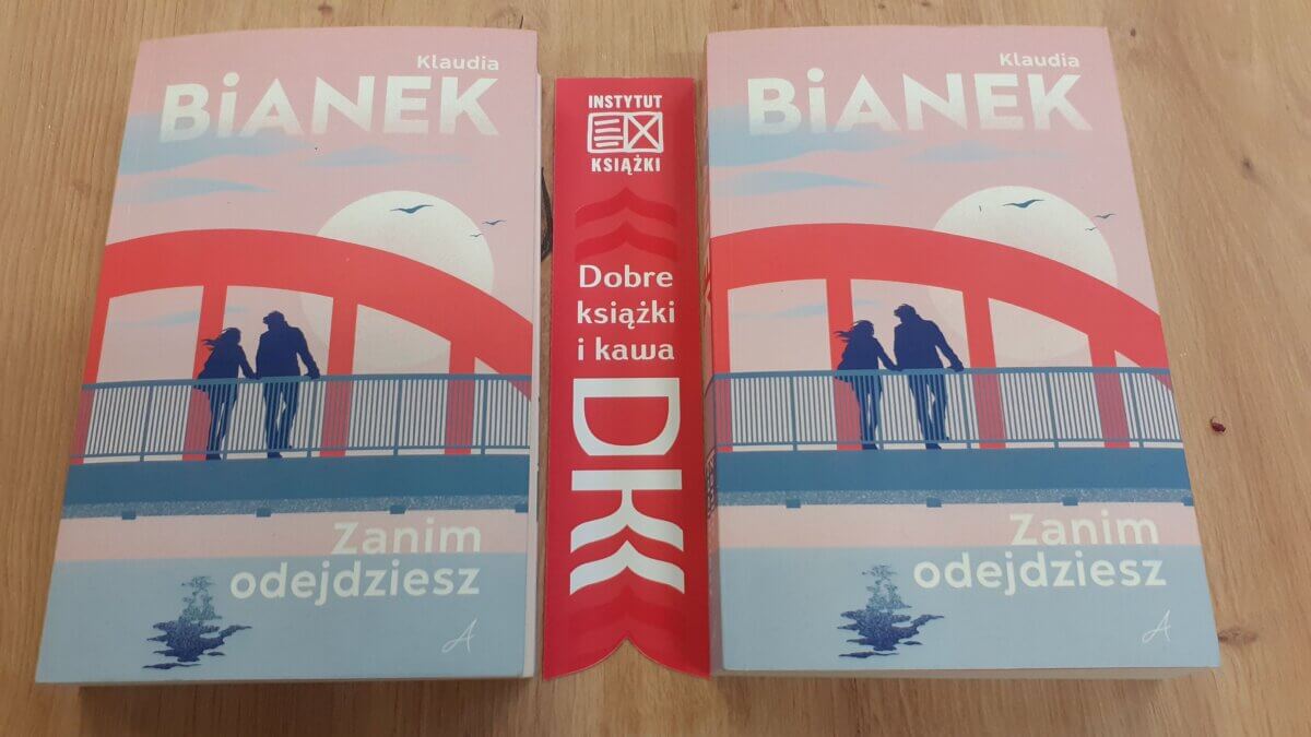 zdjęcie startowe – ekspozycja książek „Zanim odejdziesz”. Książki znajdują się na stole, obok książek leży zakładka z logiem Dyskusyjnego Klubu Książki.