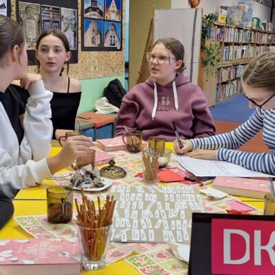 Uczestniczki DKK siedzą przy stole i dyskutują. Na stole stoją kubki z herbatą i paluszki oraz leżą książki i lista cech charakteru. Kliknięcie powoduje powiększenie zdjęcia.