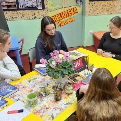 Pięć dziewczynek siedzi przy stole, rozmawiają o książce. Kliknięcie powoduje powiększenie zdjęcia.