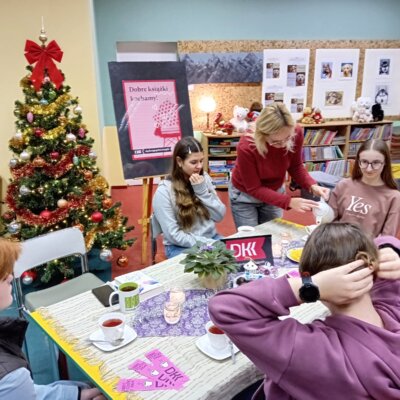 Klubowiczki siedzą przy stole. Bibliotekarka nalewa z dzbanka do filiżanek zimowy napar. Kliknięcie w obrazek spowoduje powiększenie.