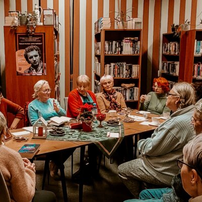 Wnętrze Filii nr 8. Trwa spotkanie literackie. Przy stole siedzi prowadząca Janina Jurgowiak oraz jedenastu uczestników wydarzenia. Kliknięcie powoduje powiększenie zdjęcia.