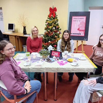 Uczestniczki młodzieżowego DKK wraz z bibliotekarką siedzą przy stole i udekorowanej choince. Kliknięcie w obrazek spowoduje powiększenie.