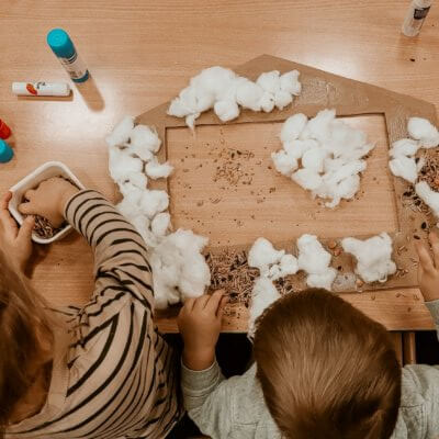 Dzieci siedzą przy stoliku i ozdabiają karmnik dla ptaków. Kliknięcie powoduje powiększenie zdjęcia.